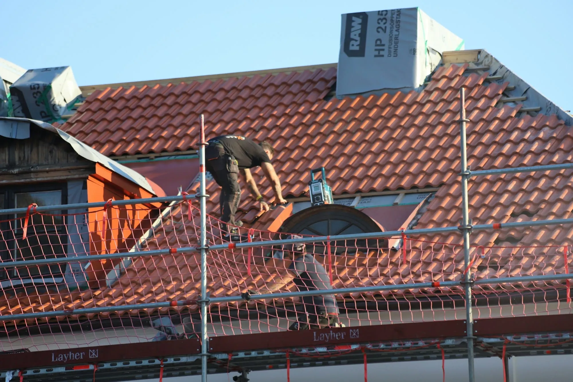 Roofer working on a tiled roof behind scaffolding